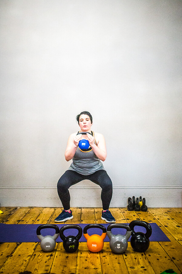 woman doing a kettle bell squat with row of kettlebells in front of her